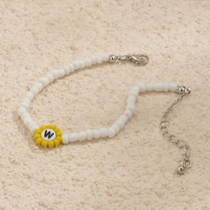 Detalle de pulsera de cuentas blancas con girasol amarillo y letra W grabada