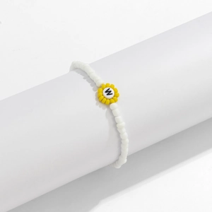 Detalle de pulsera de cuentas blancas con dije de girasol y colgante de letra W