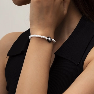 Primer plano de pulsera de cuentas blancas con un dije de flor negra y la letra N