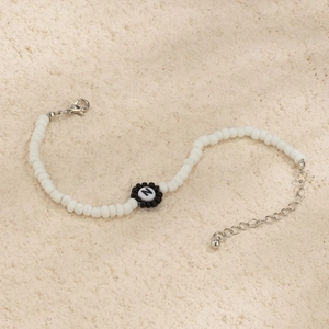Detalle de pulsera de cuentas blancas con letra N negra y cierre plateado ajustable