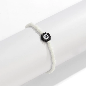 Detalle de pulsera de cuentas blancas con dije de flor en blanco y negro y la letra Z