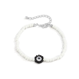 Detalle de pulsera de cuentas con perlas blancas, flor negra y dije de la letra N
