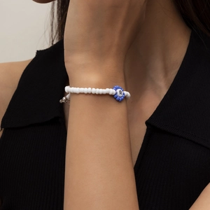 Detalle de pulsera de cuentas de colores con flor azul y letra R en la muñeca del modelo
