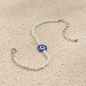 Detalle de collar de cuentas con dije de flor azul y colgante de letra R en negro