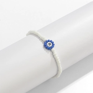 Detalle de la pulsera artesanal de cuentas blancas con flor azul y cuenta de letra R