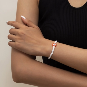 Detalle de pulsera de cuentas blancas con dije de flor naranja y letra S incorporada