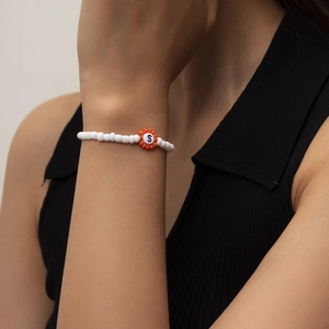 Detalle de pulsera de cuentas blancas y flor naranja con la letra S para mujeres