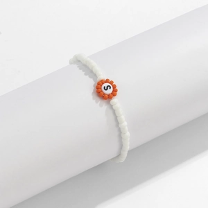 Detalle de pulsera de cuentas blancas con un dije de flor naranja y la letra S grabada