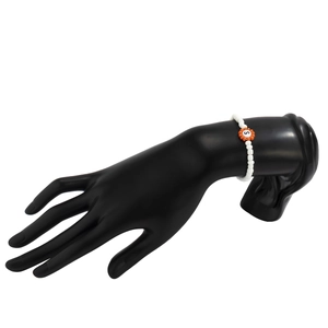 Detalle de pulsera de cuentas blancas con flor naranja y letra S negra en el centro