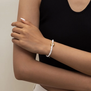 Detalle de pulsera de cuentas blancas con flor dorada y corazón rojo en la muñeca