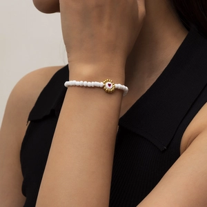 Detalle de pulsera de cuentas blancas con flor dorada y diseño de pequeño corazón rojo