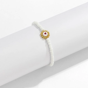 Detalle de pulsera de cuentas blancas con dije de flor dorada y corazón rojo central