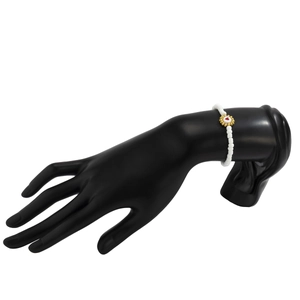 Pulsera de cuentas blancas con flor dorada y corazón rojo en un modelo de mano negro