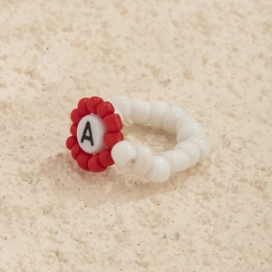 Primer plano de anillo hecho a mano con cuentas blancas y flor roja con letra A