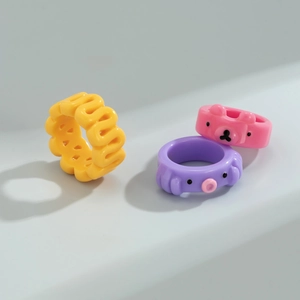 Dettaglio di anelli in resina colorata con orsetto rosa e motivi geometrici a onda