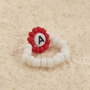 Detalle de un anillo artesanal de cuentas blancas y flor roja con el diseño de letra A