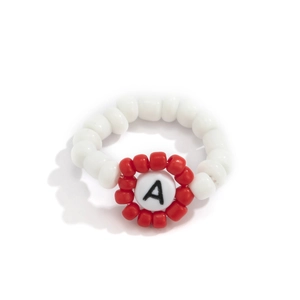 Detalle de anillo de cuentas hecho a mano con flor roja y cuenta de acrílico con la letra A