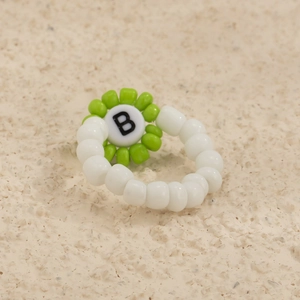 Detalle macro de un anillo de cuentas blancas hecho a mano con flor verde y letra B