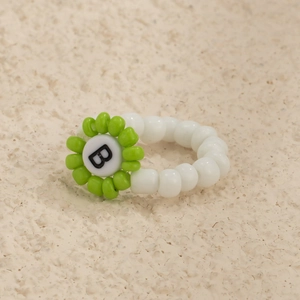 Detalle de anillo de cuentas blancas con motivo de flor verde y letra B