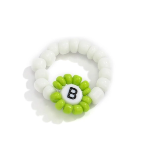 Detalle de anillo de cuentas blancas con una flor verde y la letra B grabada