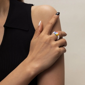 Detalle de anillo artesanal de cuentas blancas con flor de arcoíris y dije de la letra C