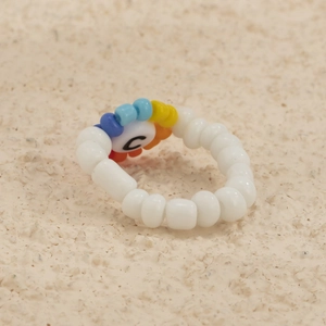 Detalle de anillo de cuentas blancas con pieza de colores y cuenta con la letra C