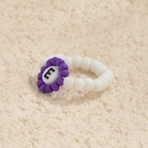 Primer plano de un anillo artesanal con perlas blancas y cuenta de flor con letra E