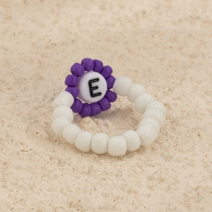 Detalle macro de anillo artesanal de cuentas con una flor morada y la letra E