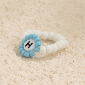 Primer plano detallado de un anillo artesanal de cuentas con flores azules y la letra H