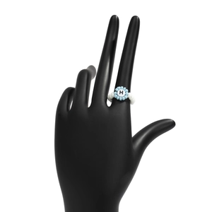 Detalle de anillo de cuentas hecho a mano con flor azul y letra H sobre soporte de mano negro