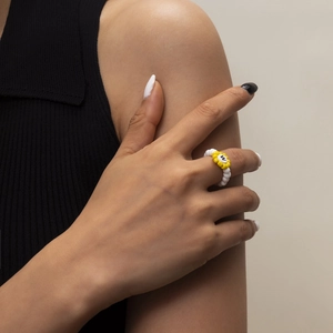Primer plano de un anillo de cuentas de colores con flor amarilla y letra W en el dedo