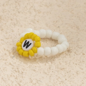 Detalle de anillo artesanal de cuentas blancas con flor amarilla y cuenta de letra W
