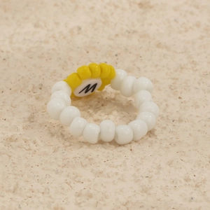 Detalle de anillo de cuentas con perlas blancas y colgante de sol amarillo con letra M