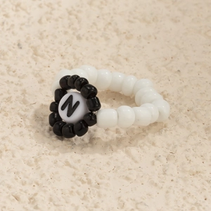 Detalle de anillo de cuentas hecho a mano con perlas blancas y letra N en negro