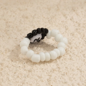 Detalle de anillo de cuentas acrílicas blancas con dije central con la letra N