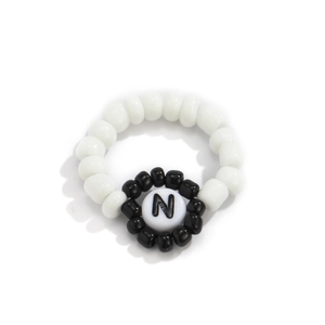 Detalle de un anillo de cuentas blancas con un dije de letra N en blanco y negro