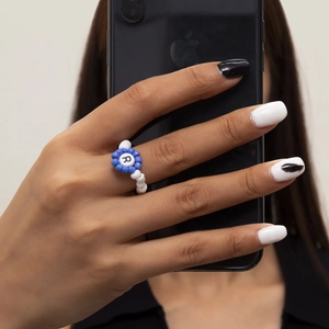 Primer plano de anillo de cuentas hecho a mano con flor azul y blanca y letra R