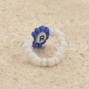 Detalle de anillo de cuentas hecho a mano con flor azul y letra R personalizada