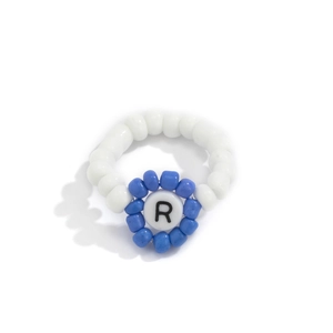 Detalle de anillo de cuentas con motivo floral azul y cuenta central con la letra R