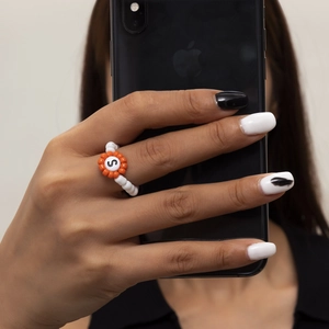 Detalle de anillo de cuentas con girasol naranja y letra S en un dedo femenino