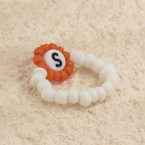 Macro de anillo de cuentas blancas con adorno naranja y letra S negra decorativa