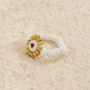 Detalle de anillo de cuentas con flor dorada y un amuleto de corazón blanco al centro