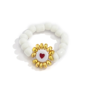 Primer plano de anillo de cuentas blancas con flor dorada y cuenta de corazón rojo