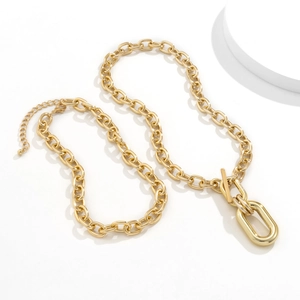 Detail of gold chunky chain necklace featuring an oversized oval toggle clasp on a white stand
