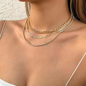 Primer plano de collares dorados con cadena cubana, eslabones de ancla y tenis con cristales