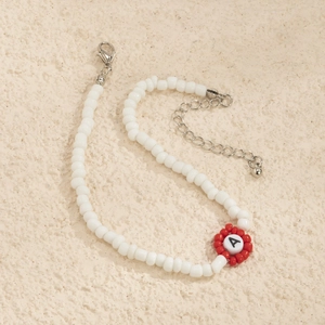 Detalle de collar de cuentas blancas con adorno de flor y colgante con la letra A