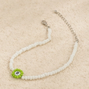Detalle de collar de cuentas blancas con flor verde y colgante con la letra B blanca