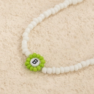 Detalle macro del collar de cuentas blancas con flor verde y colgante de la letra B
