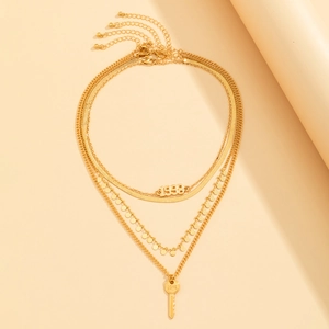 Detalle de collar dorado de varias capas con colgante 1998 y llave con grabado Love