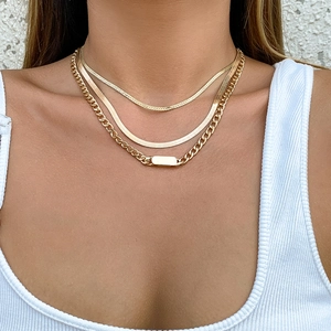 Primer plano de collares dorados en capas y elegante colgante rectangular en el cuello
